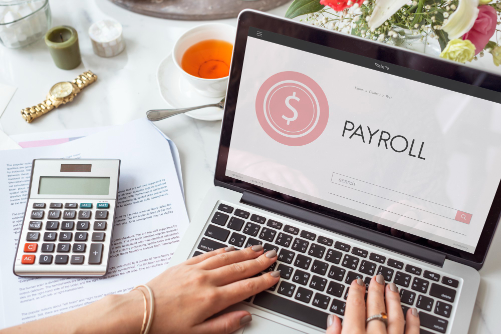 Laptop with 'PAYROLL' on screen, calculator, and financial documents, depicting comprehensive payroll management.