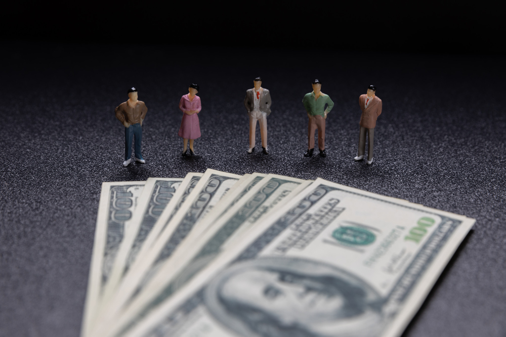 Group of miniature businessmen figures standing on piles of coins, illustrating payroll and financial management for small businesses.